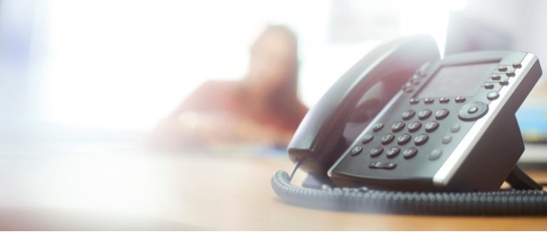 Business VoIP Phone On Desk with Blurred Woman in Background.