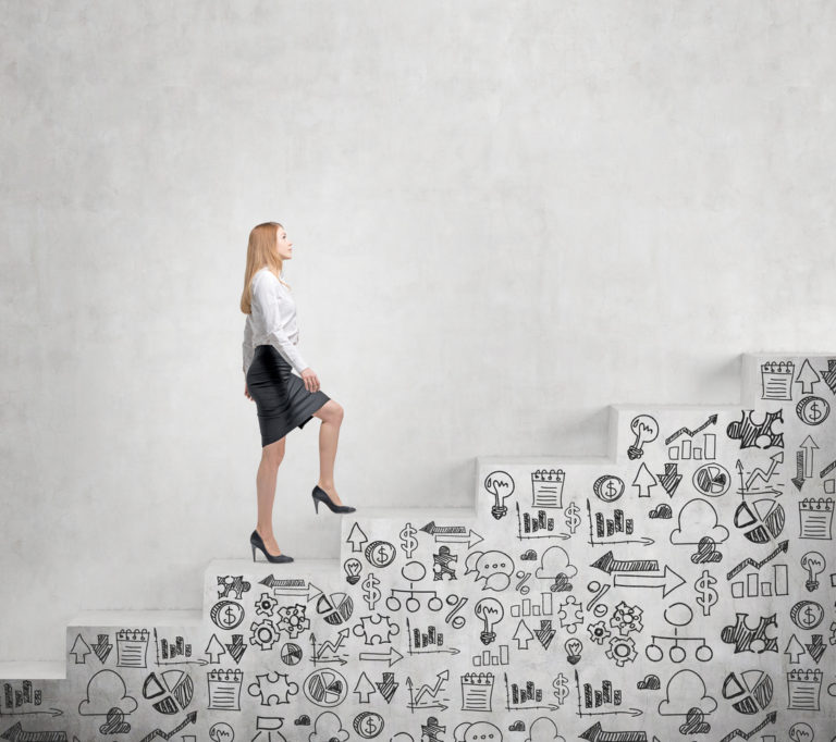 Young business woman climbing white stairs grafittied with business graphics.